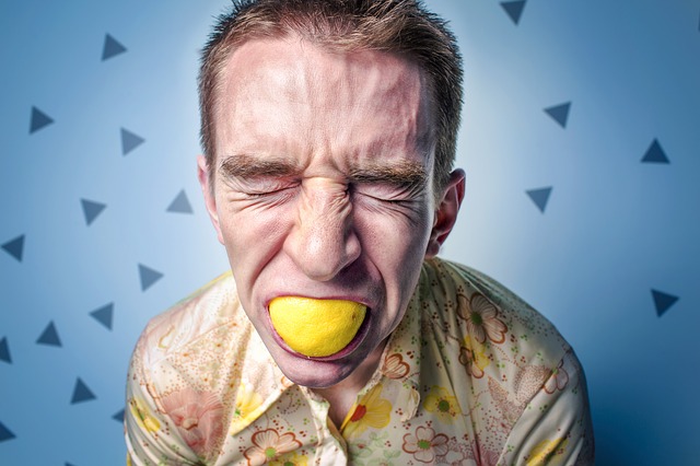 the man with the lemon in his mouth has a sour facial expression, possibly an allergic reaction to citrus