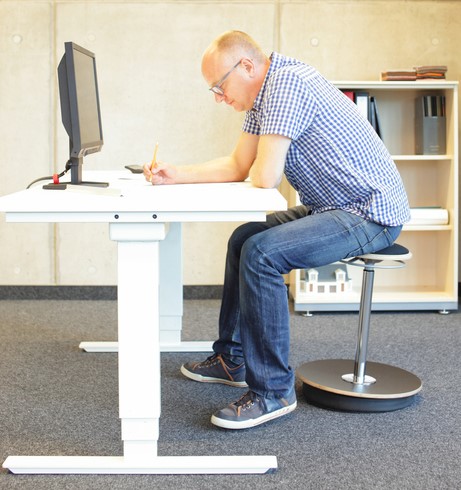 A man sits at a computer desk, he has a sedentary job.