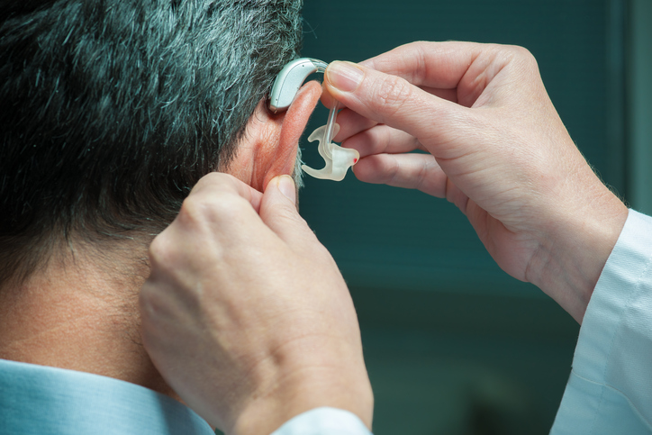 men apply a hearing aid to the ear