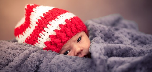 A child, lying covered, in a red and white striped cap