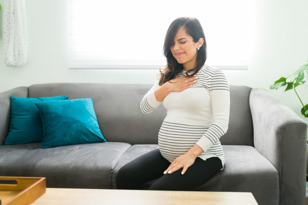 Heartburn is common in pregnant women - a pregnant woman sits on a sofa and holds her chest.
