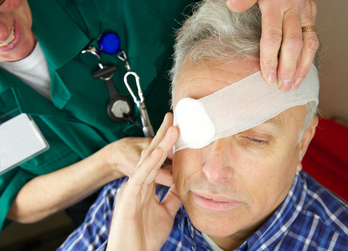 a grey man has a bandaged eye, for example after an accident, a paramedic is treating him