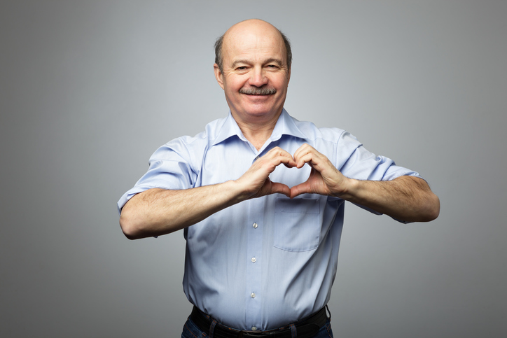 The older man has his hands on his chest in the shape of a heart, he has a happy expression on his face