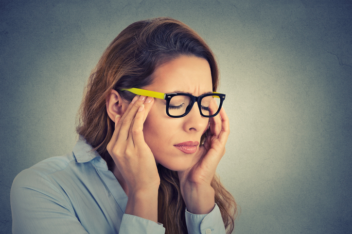 woman is having a headache and eye pains, wearing yellow glasses, with a migraine