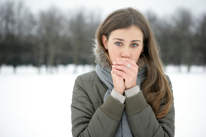 A woman warms her cold limbs with her breath, it's snowing outside, cold, cold