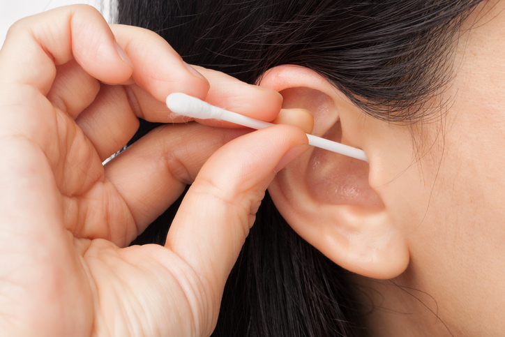 a woman cleans her ear with a cotton swab